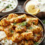 A vibrant plate featuring creamy, orange-hued butter chicken garnished with fresh coriander. The dish is served alongside fluffy basmati rice and complemented by warm naan bread, creating an inviting and colorful presentation with a rich, glossy sauce.