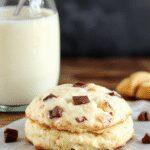 Golden-brown protein biscuits arranged on a rustic wooden board, with some broken open to reveal the soft interior and hints of oats and protein powder, garnished with a sprig of fresh herbs for a fresh touch