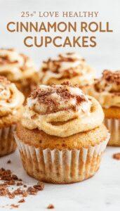 A tray of golden-brown cinnamon roll cupcakes topped with a swirl of icing, arranged on a rustic wooden surface with a soft-focus background showing cinnamon sticks and a small bowl of icing.