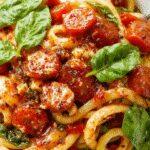 A vibrant plate of spinach and tomato pasta featuring fresh green spinach leaves, bright red cherry tomato halves, and al dente pasta strands topped with a sprinkle of grated cheese. The dish is served in a rustic white bowl on a wooden table, with a drizzle of olive oil and a few basil leaves garnish, creating an inviting and colorful presentation.