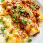 Close-up of plated healthy cheesy ground beef enchiladas featuring golden-brown tortillas filled with seasoned ground beef and melted cheese, garnished with fresh cilantro, served on a rustic plate with vibrant red sauce drizzled on top.