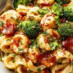 A vibrant plate of broccoli pasta featuring al dente spaghetti topped with bright green steamed broccoli florets and a sprinkle of grated cheese, garnished with fresh herbs. The dish is served on a white plate with a rustic wooden table backdrop, highlighting the colorful ingredients and inviting presentation.