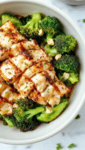 A vibrant bowl featuring grilled chicken slices nestled atop steamed broccoli florets, drizzled with a creamy garlic sauce. The dish is garnished with fresh herbs and served on a rustic wooden table, showcasing the colorful ingredients and inviting textures.