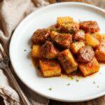 A vibrant plate featuring roasted sweet potatoes topped with slices of cooked sausage, garnished with fresh herbs. The dish showcases golden-brown sweet potatoes with caramelized edges, contrasted by the savory sausage pieces and a drizzle of honey glaze. The background is styled simply to highlight the colorful, appetizing presentation.
