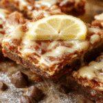 A close-up of vibrant yellow lemon brownie bars with a glossy glaze, cut into neat squares on a white plate, garnished with lemon zest and a sprig of mint, showcasing a moist, fudgy texture with a hint of citrus brightness.
