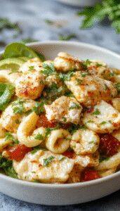 A vibrant bowl of Mediterranean chicken pasta salad showcases colorful ingredients, including grilled chicken pieces, spiral pasta, cherry tomatoes, cucumber slices, black olives, and feta cheese, garnished with fresh herbs. The salad is arranged in a rustic white bowl on a wooden surface, with some ingredients scattered around, highlighting freshness and variety.