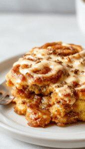 A golden-brown pumpkin cinnamon roll bake sliced to reveal swirls of cinnamon and pumpkin filling, topped with a light glaze and sprinkled with cinnamon, plated on a rustic white dish with a cozy kitchen background.