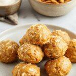 A close-up of a handful of vibrant orange pumpkin protein balls sprinkled with coconut flakes on a rustic wooden surface, arranged in a neat cluster highlighting their round shape and textured surface.