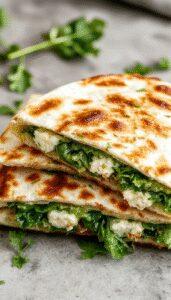 A close-up of a golden-brown quesadilla filled with vibrant green spinach and white crumbled feta cheese, sliced to reveal the gooey melted cheese and fresh spinach inside. The quesadilla is plated on a rustic wooden surface with a few fresh spinach leaves scattered around, highlighting the fresh ingredients and crispy texture.