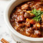 A hearty crockpot beef stew served in a rustic bowl, featuring tender chunks of beef, vibrant carrots, potatoes, and peas in a rich, savory gravy, garnished with fresh herbs. The bowl is placed on a wooden table with a folded linen napkin nearby, evoking warmth and comfort.