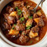 A hearty Crockpot beef stew served in a rustic white bowl, featuring tender chunks of beef, earthy carrots, potatoes, and celery immersed in a thick, savory gravy, garnished with fresh herbs, set on a wooden surface with a warm, inviting ambiance.