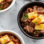 A bowl of tender shredded pot roast with chunks of caramelized pineapple and smoky chipotle sauce, garnished with fresh herbs, served with colorful roasted vegetables and a side of rice on a rustic wooden table.