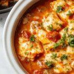 A steaming bowl of lasagna soup with layers of rich tomato broth, melted cheese, and tender pasta, garnished with fresh basil and grated Parmesan, served beside a rustic spoon on a wooden table.