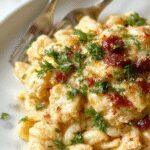 A creamy Tuscan chicken and orzo dish in a rustic white bowl, garnished with fresh herbs, showcasing tender chicken, al dente orzo, and a rich sauce, placed on a wooden table with a neutral background.